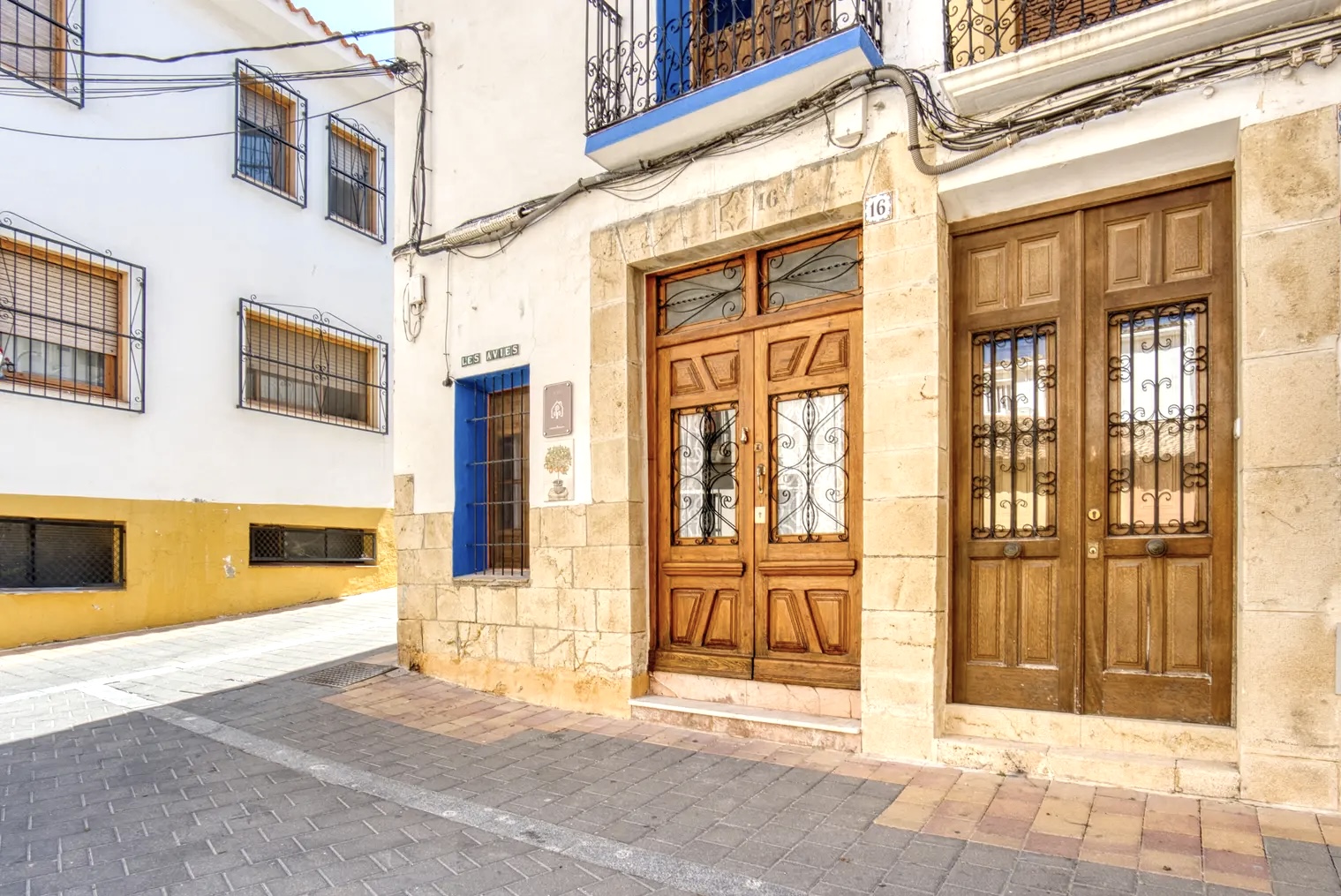 Fachada de casa tradicional en calle empedrada, con puertas de madera tallada, ventanas con rejas y detalles en piedra junto al cartel que indica 'Les Avies'.